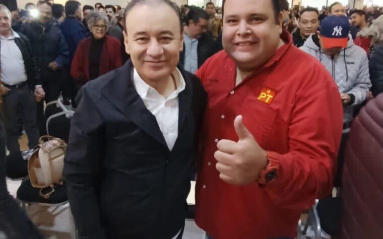 Dos asistentes posan durante un encuentro político en Hermosillo; uno viste una camisa roja con el emblema del PT